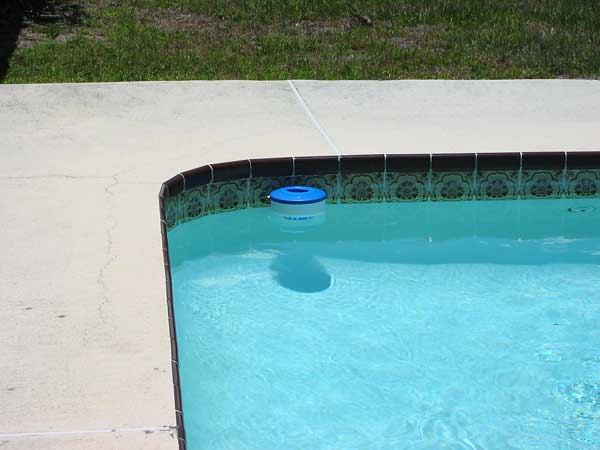 A pool float and chlorine tablets on the edge of a swimming pool. Tablets  with chlorine dispenser for swimming pools. Chlorine tablets with dosing  float, Pool float and chlorine tablets Photos